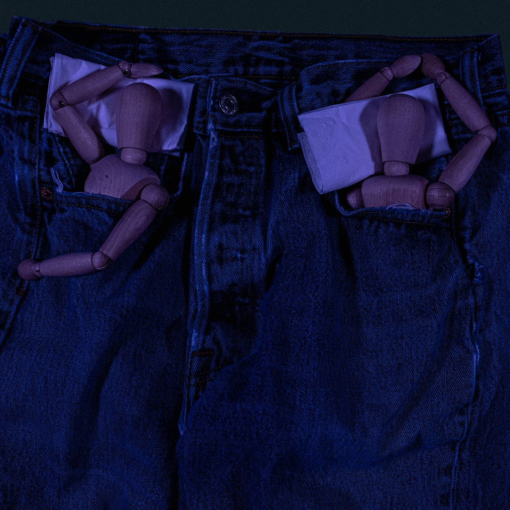 Pair of manikins, seemingly sleeping, tucked each in the pockets of a pair of jeans, using folded tissues as pillows.