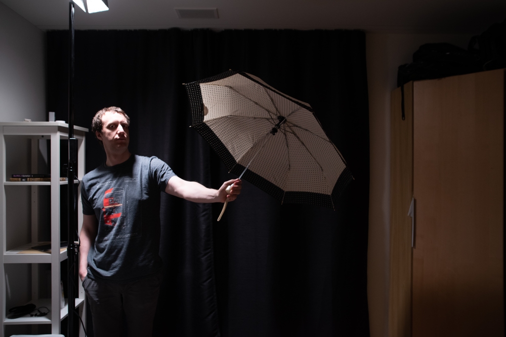 Man standing in a bedroom, holding an umbrella by its handle