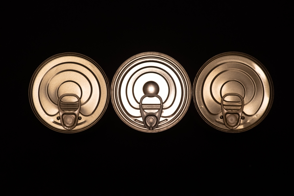 Top of three tin cans, well aligned in a row, over a black background. The left and right ones are identical, the third one is of a different model.