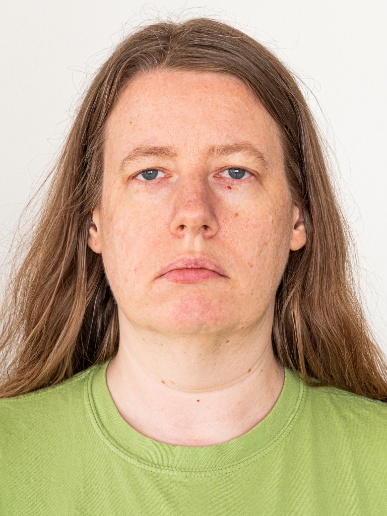 Self-portrait. The woman in the image wears a green t-shirt and has a neutral expression; the picture aspect ratio and style refer to a passport-style picture.