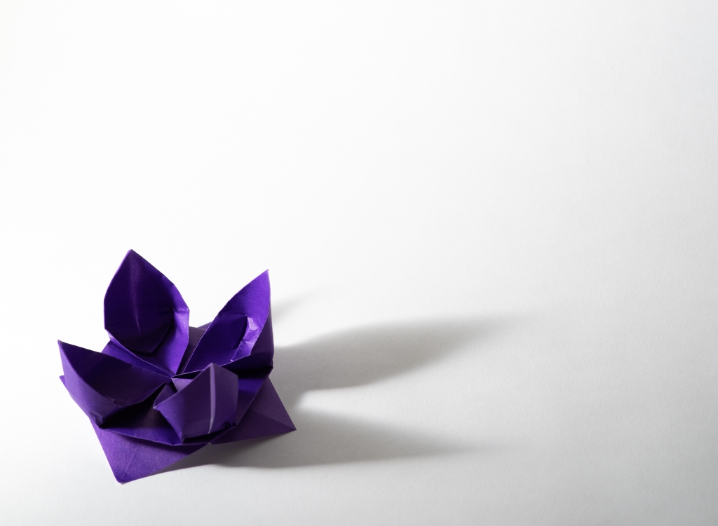 A purple origami lotus flower on a white background, with a visible soft shadow on the side.