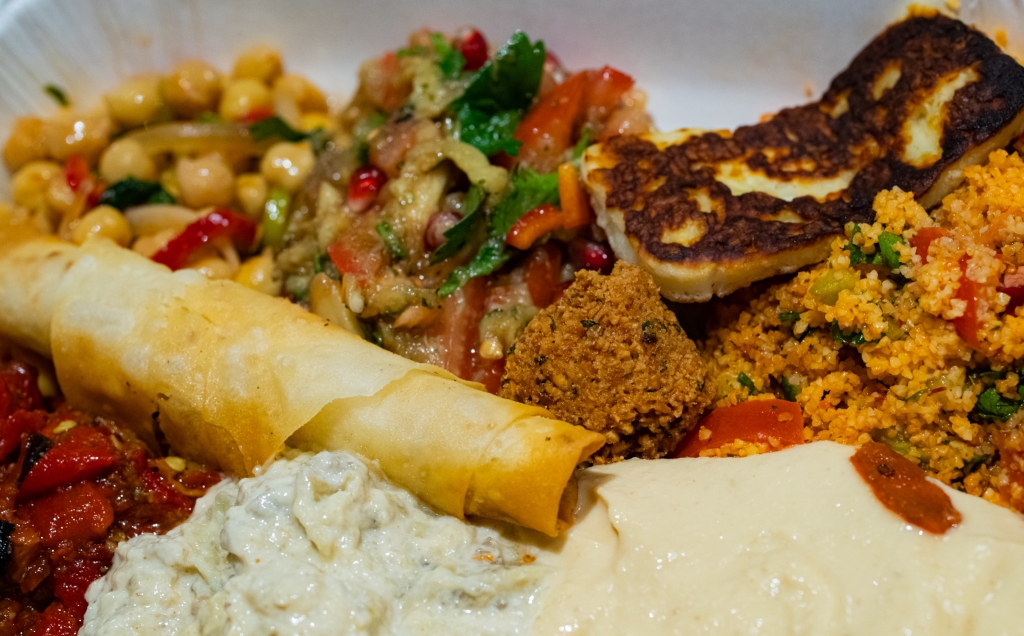 Close-up of food: hummus, falafel, various salads, baba ganoush, grilled halloumi cheese and cheese in fried phyllo